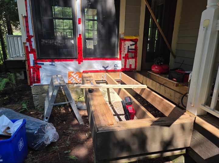 New wood frame for a deck or landing set on gravel beside a house, with house wrap taped around the windows