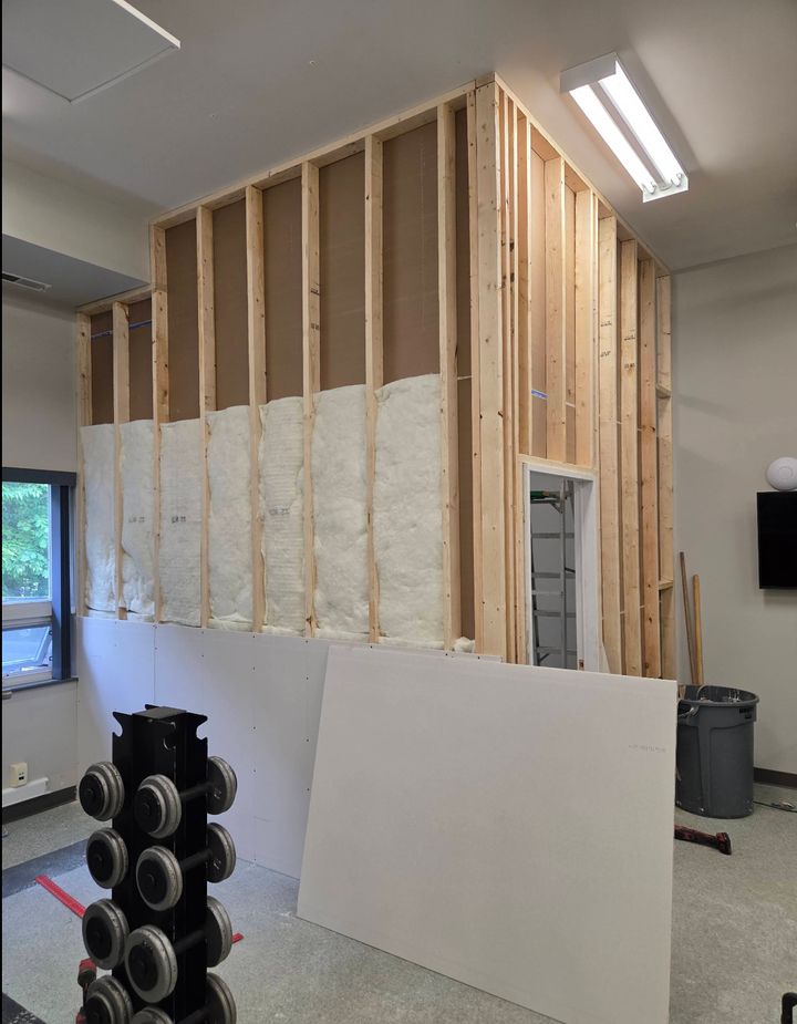 New interior wall framed with 2x4 studs and insulation batts, with a sheet of drywall leaning against it