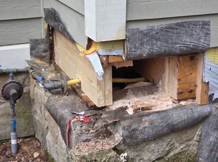 The same house corner after the repair, with new lumber framed in above the stone foundation and the gas line in place